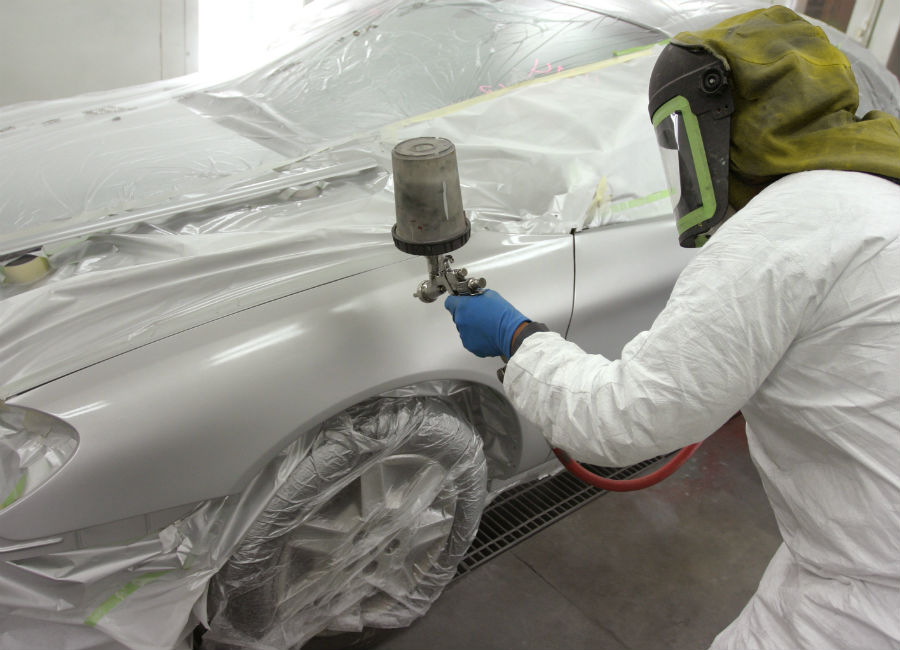 Someone spray painting the exterior of a silver coupe